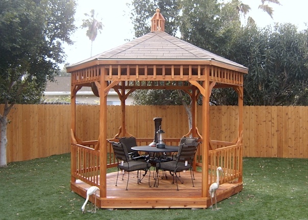 A gazebo in a back yard with table and chairs.