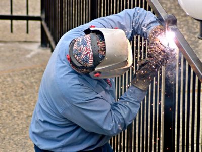 This image shows a metal fence fabricator performing welding to a black metal fence.